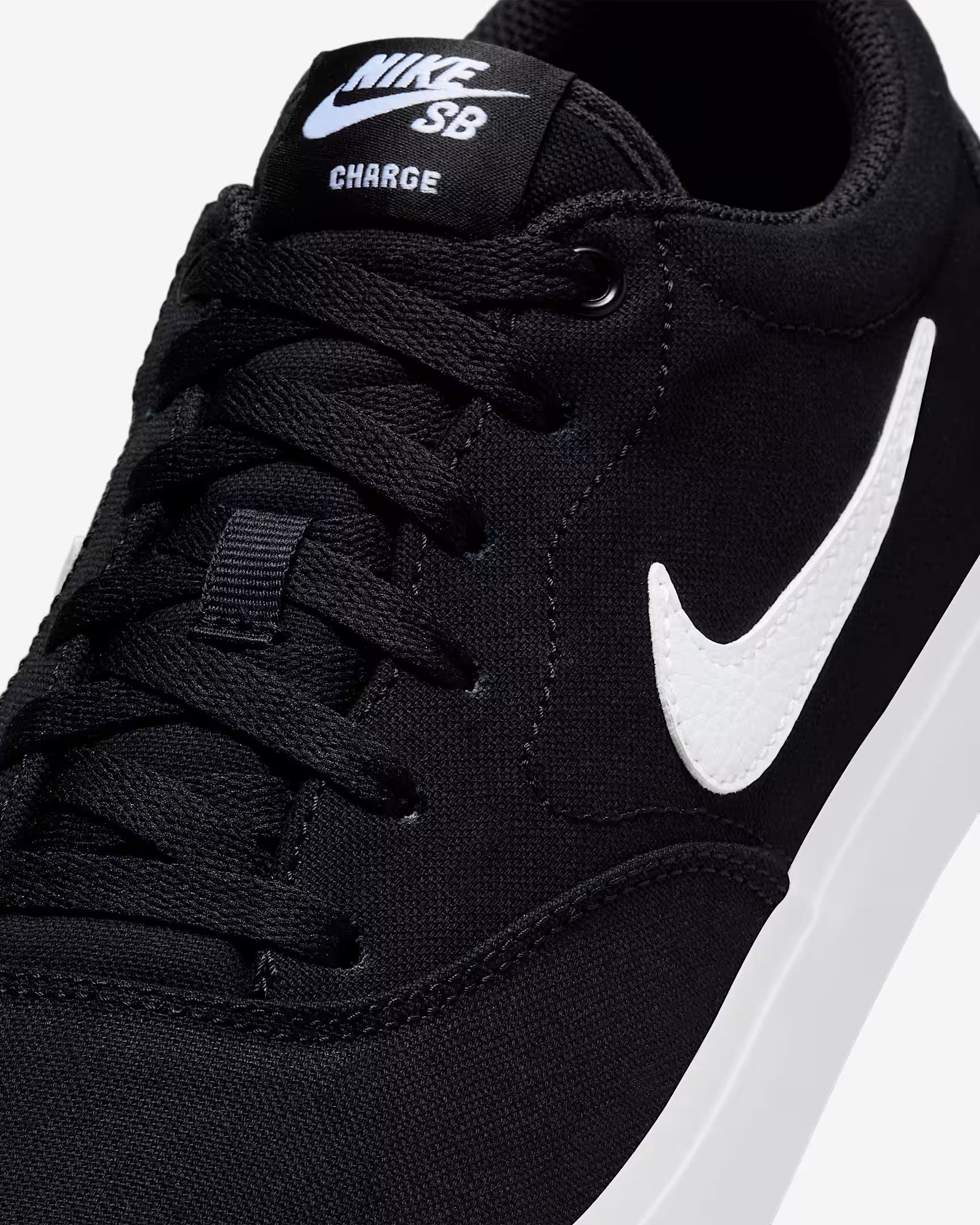 Close-up of black Nike SB Charge Canvas sneaker showing white swoosh logo, laces and canvas texture on light gray background